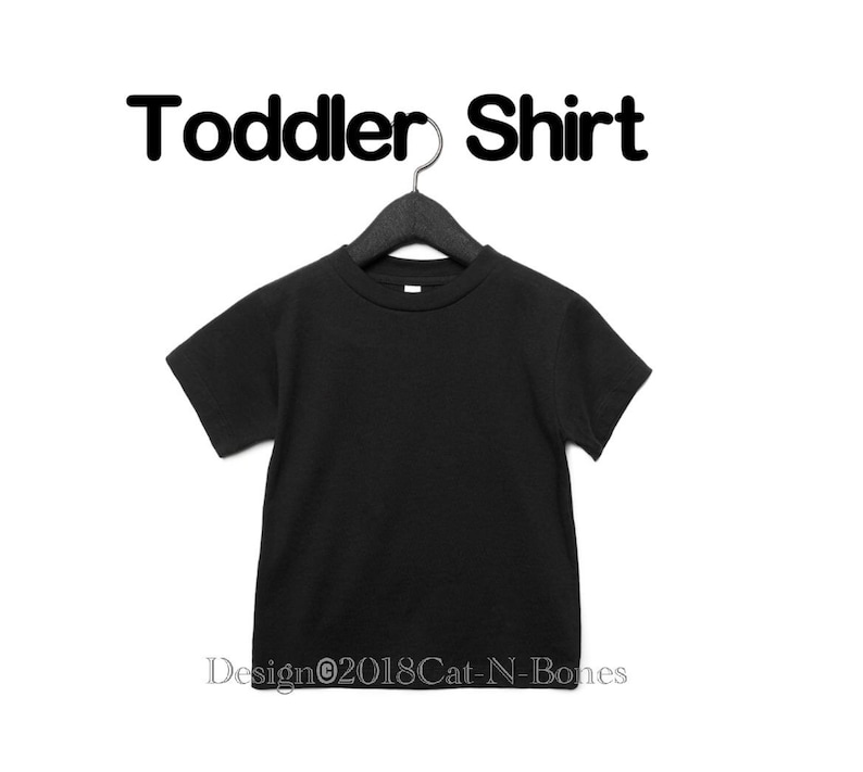 May include: Black toddler shirt hanging on a black hanger. The shirt is blank and has a crew neck. The text "Toddler Shirt" is above the shirt.