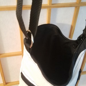 May include: White crossbody bag with black zipper accents and a black strap. The bag has two zippered pockets on the front.