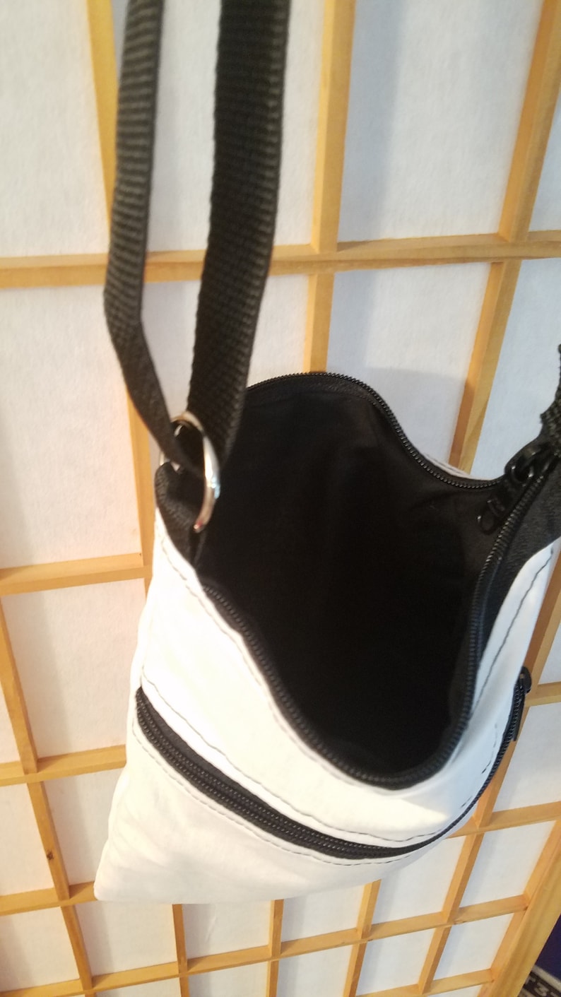 May include: White crossbody bag with black zipper accents and a black strap. The bag has two zippered pockets on the front.