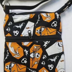 May include: Black and orange fabric crossbody bag with a zipper closure. The bag features a repeating pattern of Jack Skellington and other characters from The Nightmare Before Christmas.