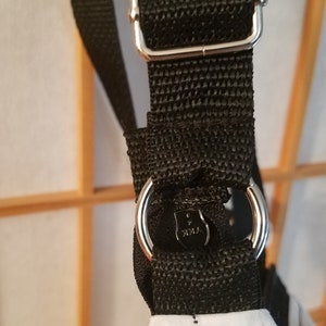 May include: Black adjustable shoulder strap with a silver buckle and a silver ring. The strap is made of a woven fabric.