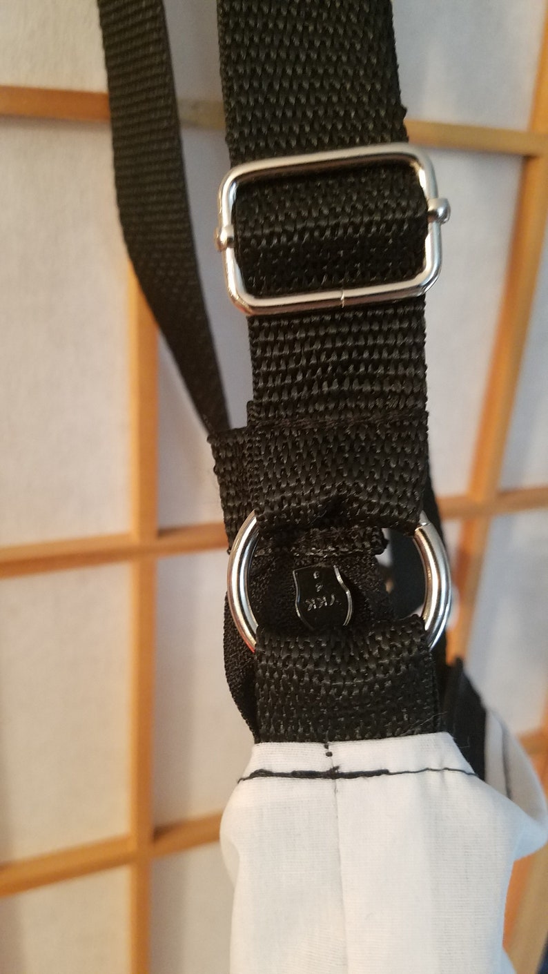 May include: Black adjustable shoulder strap with a silver buckle and a silver ring. The strap is made of a woven fabric.