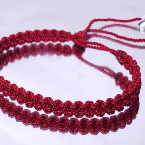 May include: A red braided bracelet with a silver heart charm and a silver bead.