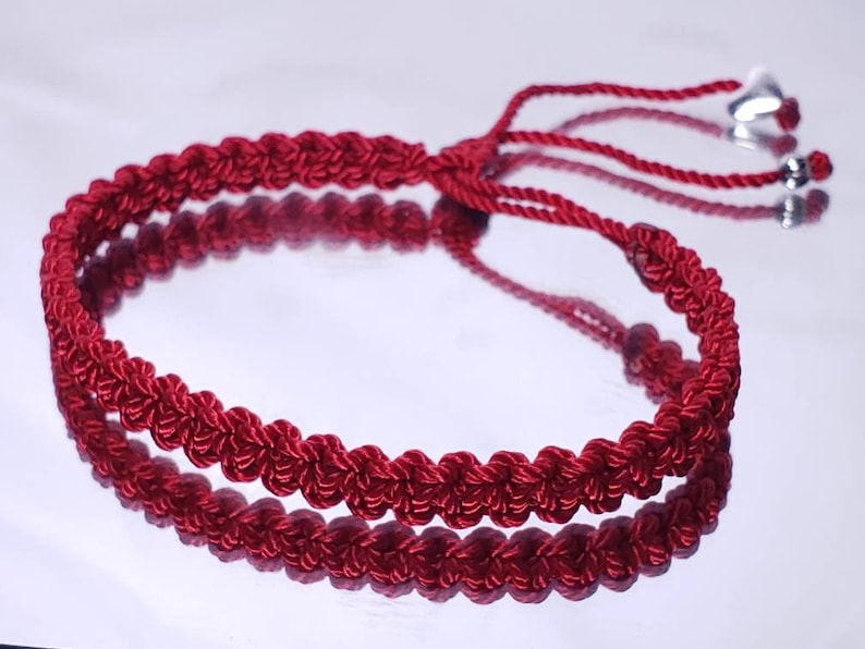 Puede incluir: Un brazalete trenzado rojo con un dije de coraz&oacute;n plateado y una cuenta plateada.