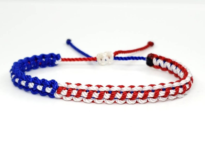 K&ouml;nnte beinhalten: Ein geflochtenes Freundschaftsarmband in Rot, Wei&szlig; und Blau. Das Armband ist mit einem gewebten Muster gefertigt und hat einen einfachen Knotenverschluss.