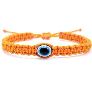 May include: Orange string bracelet with a blue evil eye charm. The bracelet is made of braided string and has a knot at the end.