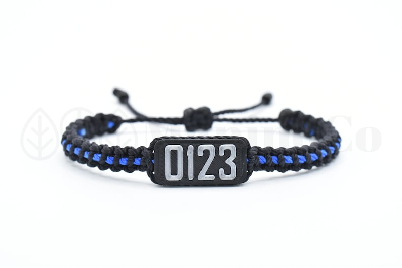 May include: Black and blue braided bracelet with a black rectangular tag that says "0123" in silver lettering.