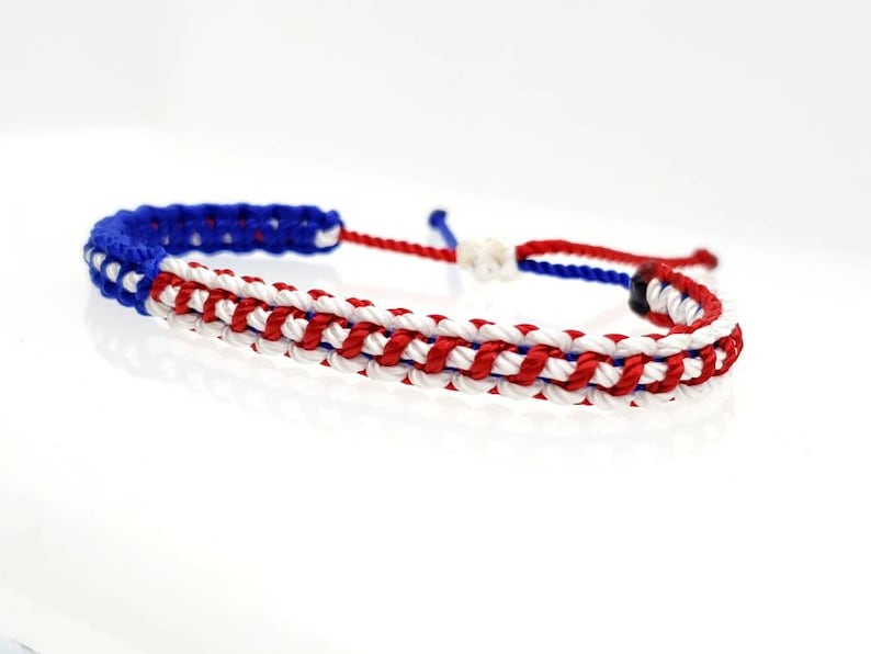 K&ouml;nnte beinhalten: Ein geflochtenes Armband in Rot, Wei&szlig; und Blau mit einem geknoteten Verschluss.