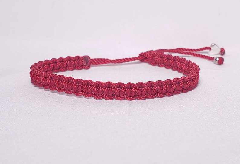 Puede incluir: Un brazalete trenzado rojo con un dije de coraz&oacute;n plateado y cierre ajustable.