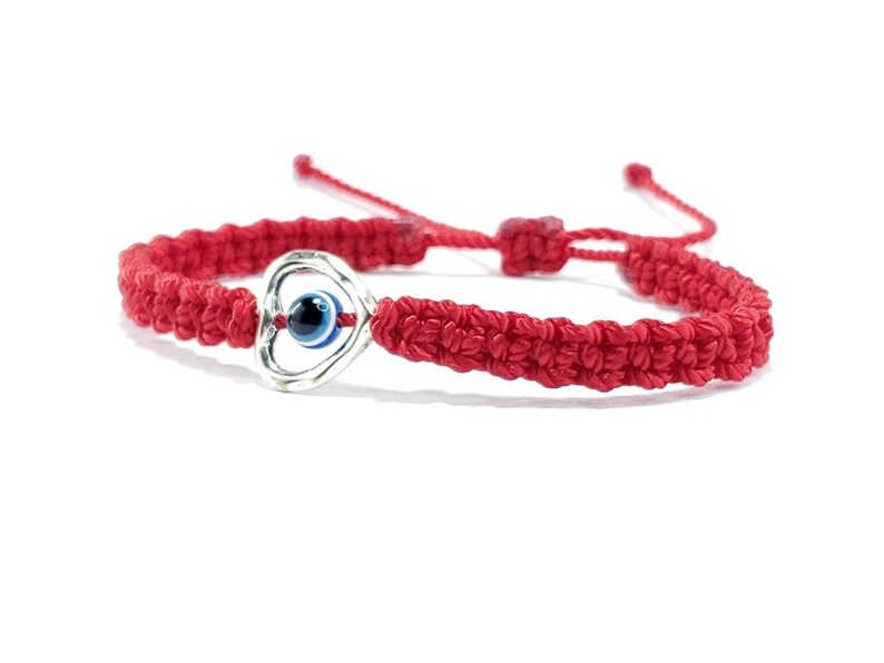 K&ouml;nnte beinhalten: Rotes Armband mit einem silbernen Herz-Anh&auml;nger mit einem blauen b&ouml;sen Auge. Das Armband ist mit einem Knoten gebunden und hat einen verschiebbaren Knoten zum Anpassen der Gr&ouml;&szlig;e.