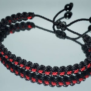 May include: Black and red braided bracelet with black beads. The bracelet is adjustable with a sliding knot.