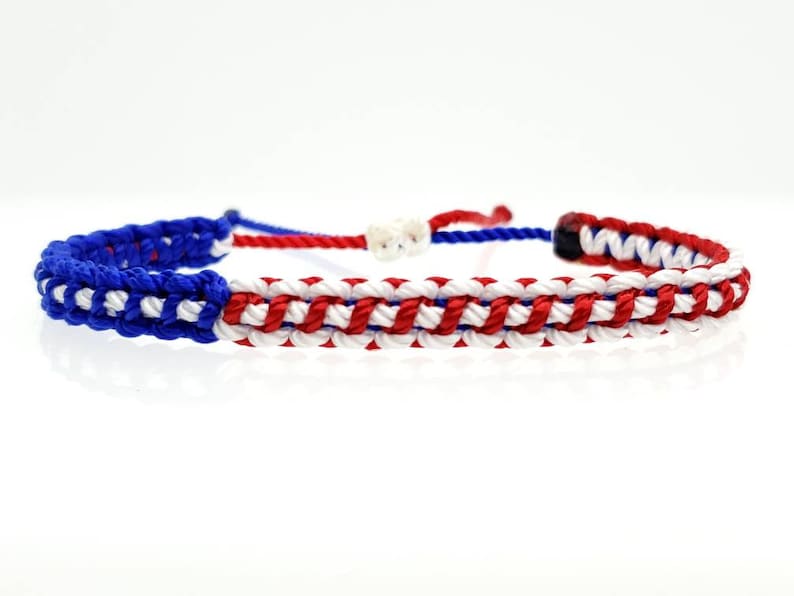 K&ouml;nnte beinhalten: Ein geflochtenes Freundschaftsarmband in Rot, Wei&szlig; und Blau. Das Armband ist mit einem gewebten Muster gefertigt und hat am Ende einen Knoten.