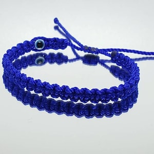 May include: A blue braided bracelet with a blue evil eye charm. The bracelet is tied with a knot and has a long string for adjusting the fit.