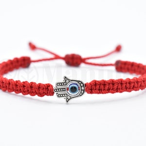 May include: Red string bracelet with a silver Hamsa hand charm with a blue evil eye in the center.