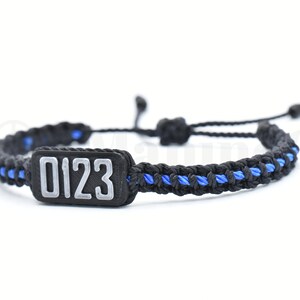 May include: Black and blue braided bracelet with a black rectangular tag that says "0123" in white.