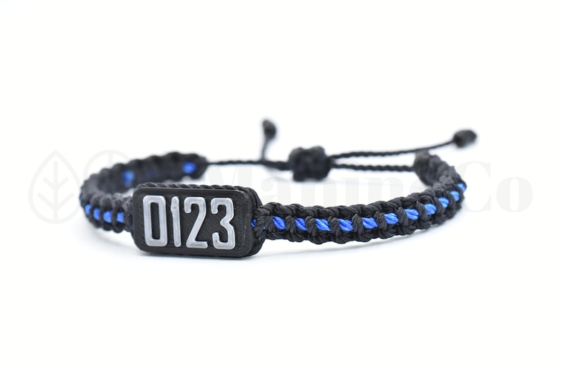 May include: Black and blue braided bracelet with a black rectangular tag that says "0123" in white.