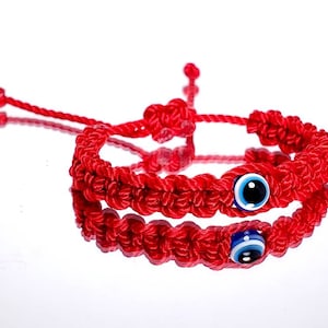 May include: Two red string bracelets with blue evil eye charms. The bracelets are knotted and have a simple design.