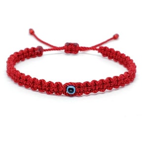 May include: Red string bracelet with a blue evil eye charm. The bracelet is knotted and has a sliding knot for adjusting the size.