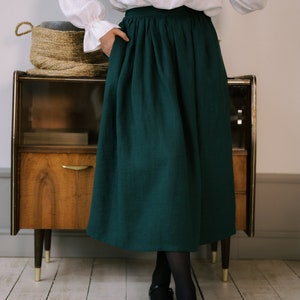 Pode incluir: Uma saia midi verde escura com cintura franzida. A saia &eacute; feita de tecido de linho e tem um caimento casual e relaxado.