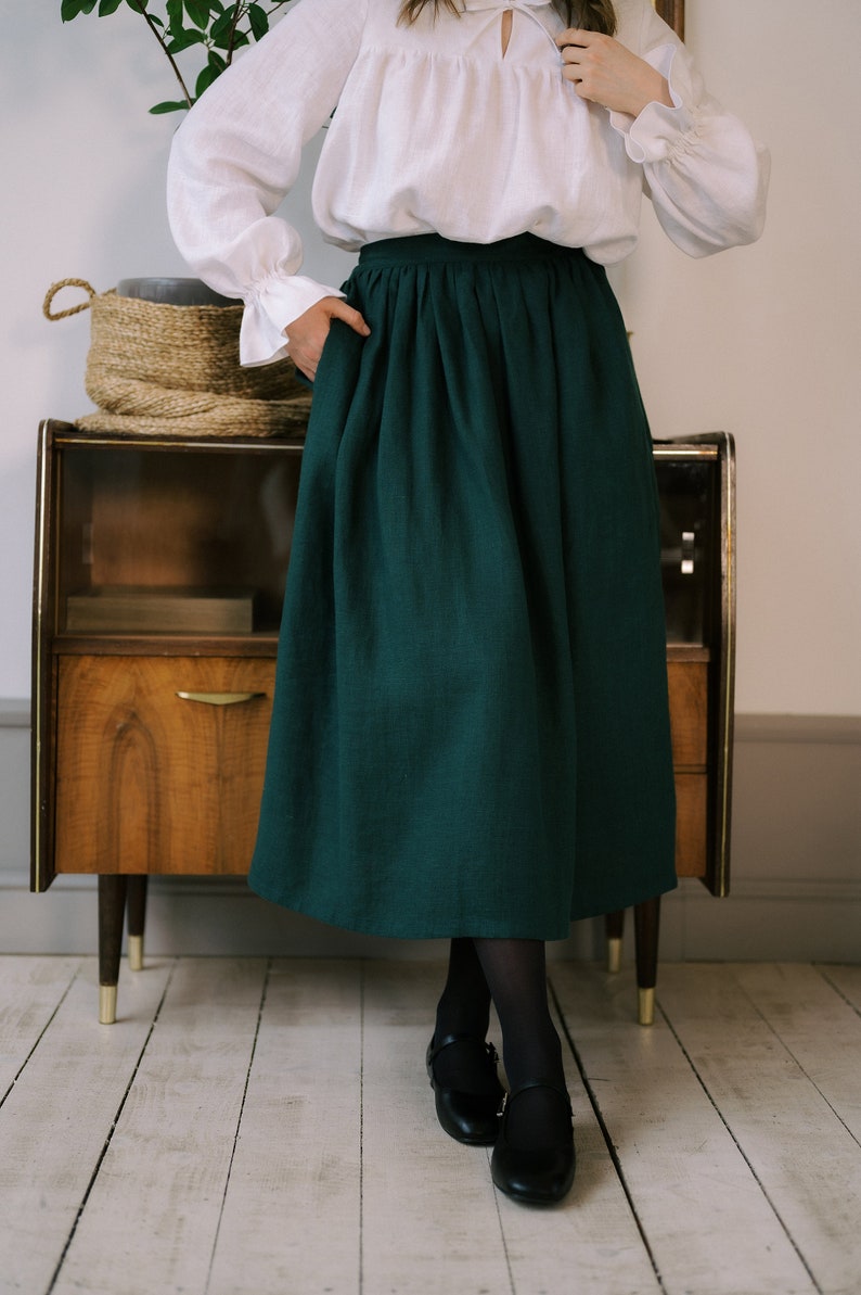 Pode incluir: Uma saia midi verde escura com cintura franzida. A saia &eacute; feita de tecido de linho e tem um caimento casual e relaxado.
