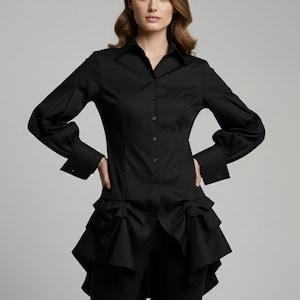May include: A black button-down shirt with long sleeves and a unique ruffled peplum design. The shirt has a classic collar and buttoned cuffs. The model is wearing black pants. This is a formal top.