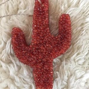 May include: A red cactus-shaped car air freshener made of small beads.