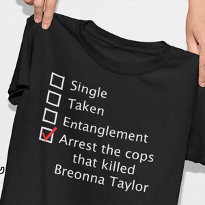 May include: Black t-shirt with white text. The text reads "Single, Taken, Entanglement, Arrest the cops that killed Breonna Taylor." The word "Entanglement" is checked with a red checkmark.