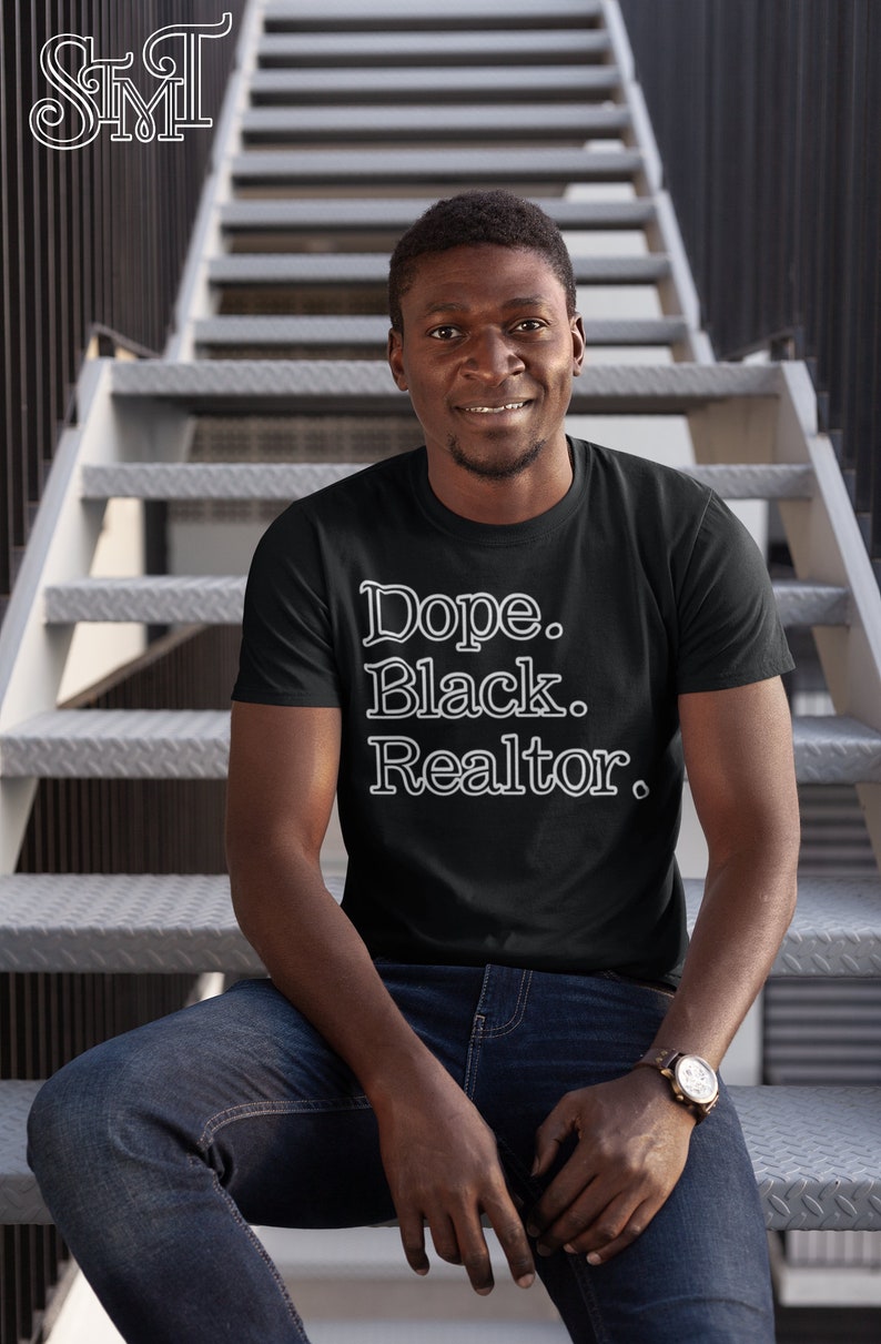 May include: Black t-shirt with the text "Dope. Black. Realtor." in a white, stylized font. The person in the image is wearing blue jeans and a watch with a brown leather band. The background is a metal staircase.