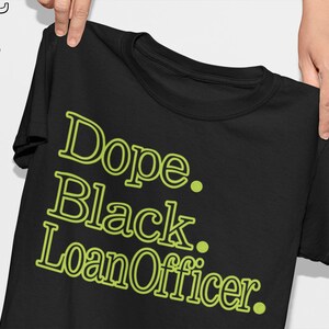 May include: Black t-shirt with the words "Dope. Black. Loan Officer." in a lime green font. The shirt is held up by a person's hands, showcasing the design. The shirt has a crew neck.