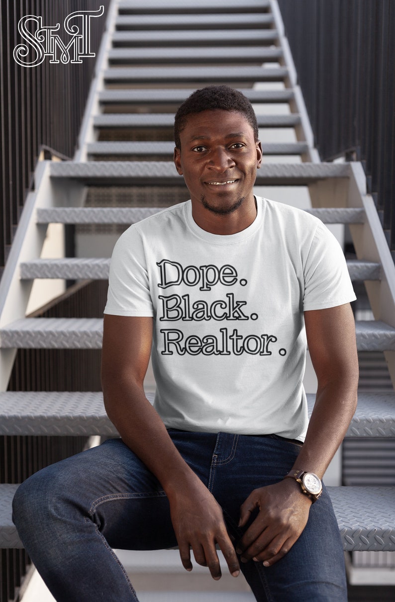 May include: White t-shirt with the text "Dope. Black. Realtor." in a black, bold font. The person is wearing blue jeans and a watch with a brown leather strap. The background is a metal staircase.