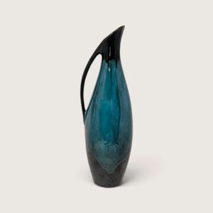 May include: A tall, slender ceramic pitcher featuring a glossy finish that transitions from a deep, dark charcoal at the base to a vibrant, mottled teal blue in the center, topped with a solid black neck and a curved, elongated handle.