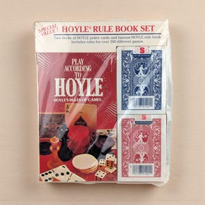 May include: A Hoyle Rule Book Set, packaged in clear plastic, includes a rule book and two decks of playing cards. The book cover is red with the text "PLAY ACCORDING TO HOYLE." One deck is blue, the other red, both with a USA guarantee.