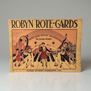 May include: Vintage "ROBYN ROTE-CARDS" book cover. The cover features a musical staff with children in costumes dancing on a piano keyboard. Text includes "TEACHING MUSICAL NOTATION WITH PICTURE SYMBOLS" and "By Louise Robyn". Published by Oliver Ditson Company, Inc.