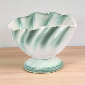 May include: A ceramic bowl with a pedestal base. The bowl has a wavy rim and a spiral design in shades of white and green. The bowl is likely used for serving desserts or displaying decorative items.