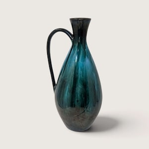 May include: A tall, teardrop-shaped ceramic pitcher featuring a glossy glaze that transitions from a deep, dark black at the neck and base to a vibrant, luminous teal blue in the center, complete with a single curved handle on the side.