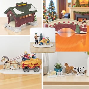 May include: A collection of miniature Christmas village figurines. The set includes a red covered bridge with a snow-covered roof, a brick bridge with lights, and a horse-drawn hay wagon. Other figurines include people, animals, and a small evergreen tree.