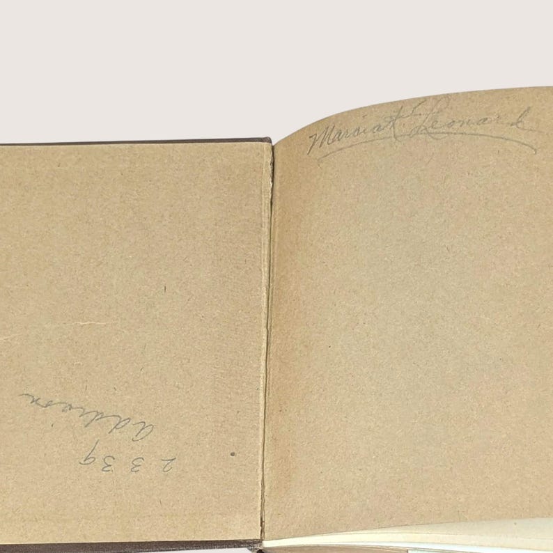 May include: Open book with aged, tan-colored pages. The right page features the handwritten name "Marcia Leonard" in cursive. The left page has the handwritten text "Addison" and the numbers "2339".