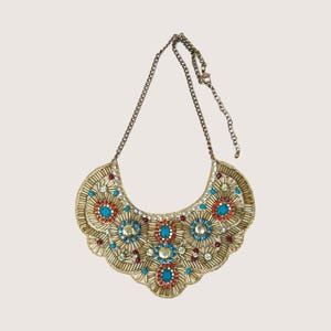 May include: A gold-toned statement necklace with a bib-style design. The necklace features turquoise, red, and silver-colored embellishments, and is strung on a delicate chain.