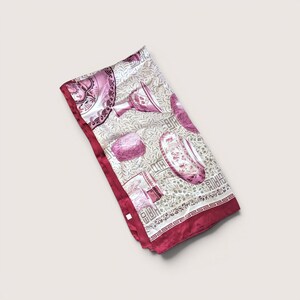 May include: A rectangular silk scarf featuring a repeating cream and beige botanical leaf pattern. The scarf is decorated with magenta illustrations of various ornate ceramic vessels and bowls, finished with a solid magenta border and a Greek key trim.