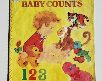 May include: A vintage children's book titled "Baby Counts" with a yellow cover. The cover features illustrations of a child, a monkey, a tiger, a lion, a bird, and a hippo. The numbers 1, 2, 3, 4, and 5 are also displayed.