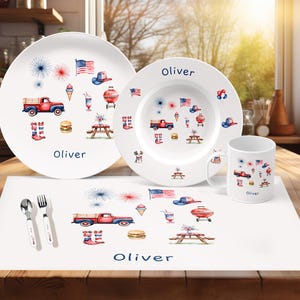 May include: A white dinnerware set with a patriotic theme, featuring a plate, bowl, and mug. Each piece is decorated with red, white, and blue illustrations of a truck, flag, and fireworks. The name "Oliver" is printed on each item.