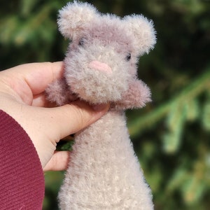 May include: A handmade plush toy in the shape of a small animal, possibly a bunny or a mouse. The toy is primarily a soft, fluffy off-white color with accents of light pink and lavender. It has small, rounded ears and a tiny pink nose.