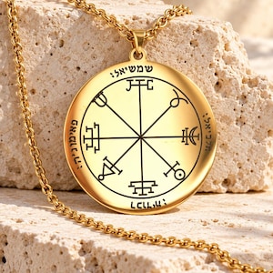 Könnte beinhalten: Eine goldfarbene, kreisförmige Anhängerkette mit einem zentralen, schwarz gravierten geometrischen Siegeldesign, das strahlenförmige Linien und verschiedene Symbole zeigt. Der Anhänger hängt an einer passenden goldfarbenen Kette mit hebräischer Schrift.