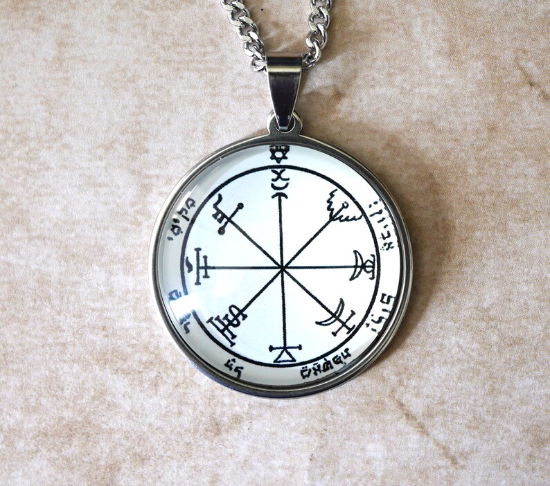 May include: A round pendant necklace with a silver-colored chain. The pendant has a white background with black symbols and text. The pendant is encased in a silver-colored metal frame.