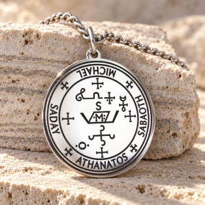 May include: A circular silver-toned pendant on a matching metal chain. The pendant features an engraved design with the text MICHAEL, SADAY, SABAOTH, and ATHANATOS around the perimeter, surrounding a central symbol with the letter M.