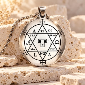 Könnte beinhalten: Ein runder silberfarbener Metallanhänger an einer passenden Kette mit einer eingravierten sechsstrahligen Sternform. In der Mitte befindet sich ein T-förmiges Symbol, umgeben von den Buchstaben A, TE, G, RAM, TON, MA, L, A, TRA und Symbolen wie Omega.