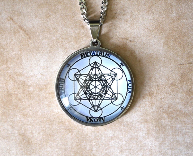 K&ouml;nnte beinhalten: Ein runder silberfarbener Anh&auml;nger mit einer schwarz-wei&szlig;en geometrischen Metatron-W&uuml;rfel-Grafik unter einer Glaskuppel. Der kreisf&ouml;rmige Rahmen enth&auml;lt die Schriftz&uuml;ge METATRUN, HUHA, PUIA und AONA um das zentrale geometrische Symbol.