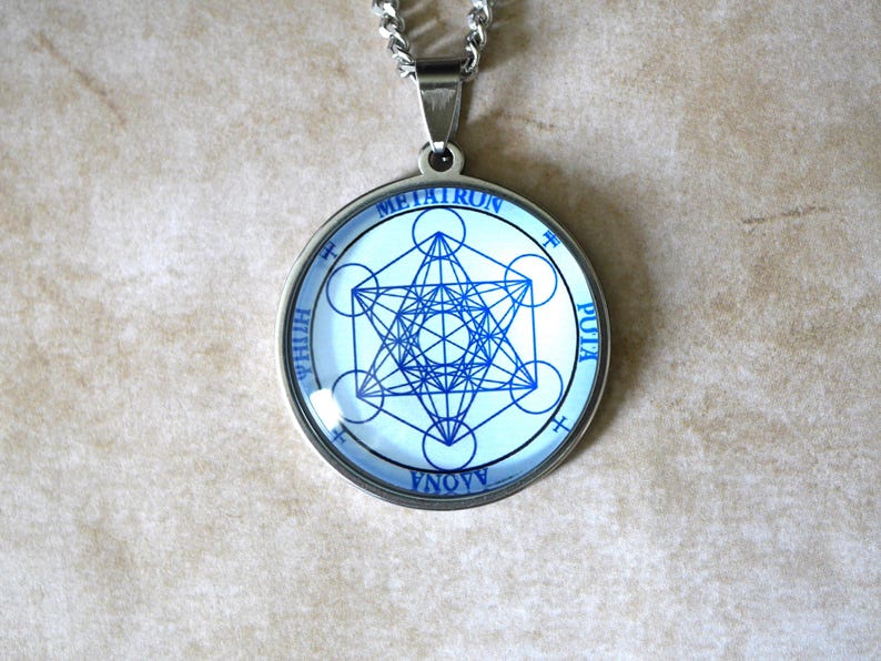 K&ouml;nnte beinhalten: Ein kreisf&ouml;rmiger silberfarbener Anh&auml;nger mit einem blauen geometrischen Metatron-W&uuml;rfel-Design auf wei&szlig;em Hintergrund. Der Text METATRON ist oben aufgedruckt, mit zus&auml;tzlichem Text entlang des Umfangs des kreisf&ouml;rmigen Rahmens.
