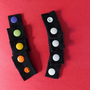 May include: Two sets of black fabric squares with colorful and white buttons. The buttons are sewn onto the fabric squares.