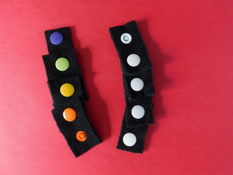 May include: Two sets of black fabric squares with colorful and white buttons. The buttons are sewn onto the fabric squares.